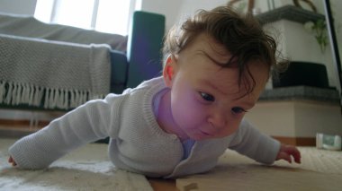 Bebek yerde yatıyor, kollarıyla yukarı itiyor, çevreyi keşfediyor, merakla bekliyor, oyuncaklarla çevrili bir evde, emeklemeyi öğrenmenin ilk aşamalarında.