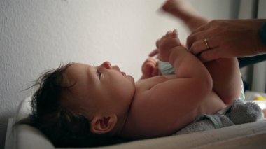 Bebek masasını değiştiriyor, anne kucağında bebek bezi, çocuk hafifçe gülümsüyor, rutin bakım, her gün ebeveyn ile etkileşim, rahatlık ve bakım, yakın ilişki..