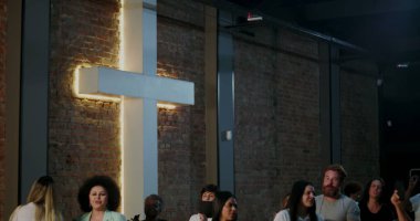 İbadet eden bir grup insan kilisenin içinde büyük aydınlatılmış haç yakınında toplandı. Barışçıl ve huzurlu bir ortamda birlik, inanç ve ruhsal bağlantıyı yansıtıyorlar.