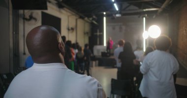 Cemaatin ayakta durduğu ve ibadet ettiği geniş bir kilise ayini sahnedeki insanların arka planı, modern kilise iç mimarisi, inanç birliği.