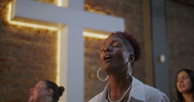 Tutkulu bir şekilde ibadet eden bir kadın, maneviyat ve inançla anlamlı ve duygusal bir bağ içinde, dua eden bir kilise cemaati ve aydınlatılmış bir haçla.