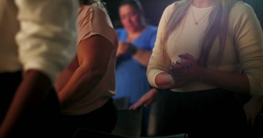 Manevi bir buluşmada el çırpan kadın, düşünceli ifade, ibadet ortamında çeşitli insanlarla çevrili, sadakat, inanç ve topluluk bağlantısına odaklanmış.