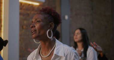 Huzurlu bir ifadeyle şarkı söyleyen bir kadın, bir kilise ayini sırasında ruhaniliğe ve inanca dalmış, arka planda aydınlatılmış bir haç