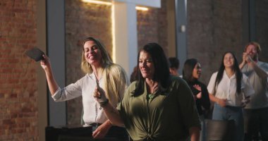 Kiliseye ibadet sırasında bağış kutusuna zarf koyan iki kadın, neşeli ve saygılı ifadeler, ruhani sunuma katılan çeşitli arka planda yer alan farklı topluluk