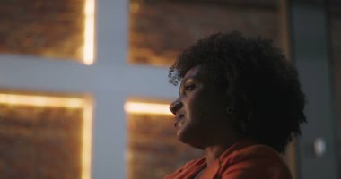 Kıvırcık saçlı bir kadın, kilisede aydınlanmış bir haçın önünde derin bir ibadete dalmış, ruhani bağlantı, inanç, tefekkür, dua anı.