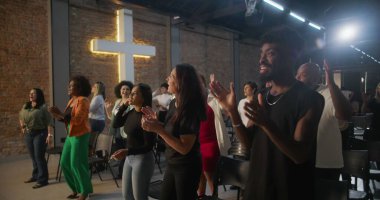 Kilisede ibadet sırasında alkışlayan ve gülümseyen çeşitli insanlar, arka planda parlayan haç, neşe, birlik ve ruhsal bağlantı ifadeleri