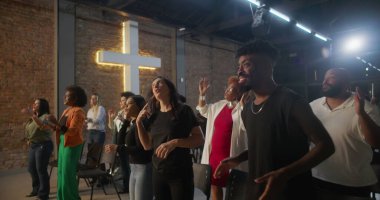 Kilisede ibadet sırasında alkışlayan ve gülümseyen çeşitli insanlar, arka planda parlayan haç, neşe, birlik ve ruhsal bağlantı ifadeleri