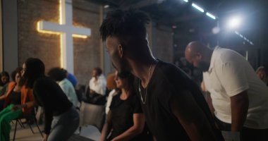 Kilise ayini sırasında oturan cemaat, arka planda aydınlatılmış haçla dikkatle dinliyor, inanç ve ruhsal bağlantı için çeşitli topluluklar bir araya geliyor.