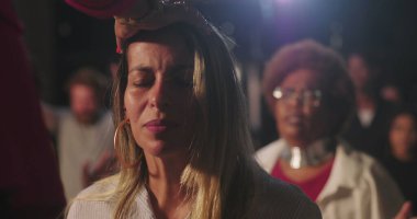 Vaiz kadını ruhani törenle kutsadı, gözleri kapalı, derin tapınma ve inanç, duygusal bağlılık anı çeşitli Hıristiyan ayinleriyle çevrili.