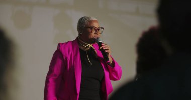 Sözcü tutkulu bir şekilde dinleyicilere hitap ediyor, mikrofonu tutuyor, vurgu için elini işaret ediyor, güçlü vaaz dağıtımı, çeşitli cemaatler dikkatlice dinliyor, ruhani olay