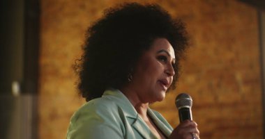 Podyumda tutkulu bir şekilde mikrofona konuşan bir kadın, ruhani dinleyicilere ilham verici bir mesaj veriyor, kendine güvenen bir lider ve inanç toplantısı sırasında güçlü bir bağlantı kuruyor.