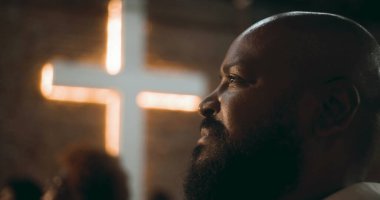 İbadet sırasında düşünceli ifadeli bir adamın profili, arka plan, inanç, maneviyat ve içgözlem konularında aydınlatılmış bir haç.