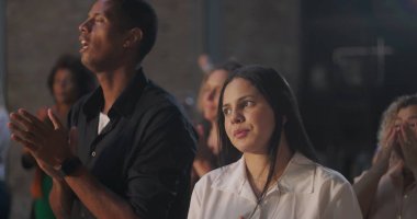 İbadet eden farklı bireyler, barışçıl ifadeyle odaklanmış genç bir kadın, grup el çırpıyor ve dini ortamda, inançta ve ruhsal bağlantıda şarkı söylüyor.