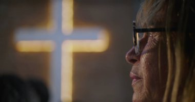 İbadet sırasında huzur içinde dua eden yaşlı kadın, arka plan, inanç, maneviyat ve içgözlem konularında aydınlatılmış haç,