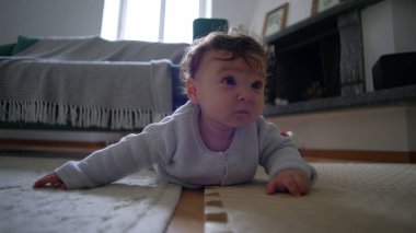 Bebek yerde yatıyor, meraklı bir ifadeyle bekliyor, ağırlığı kollarıyla tutuyor, emeklemenin ilk aşamaları, rahat bir yuva kurma, meraklı ve odaklanmış..