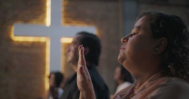 Çeşitli grup ibadetleri sırasında elleri kalbimde olan kadın, arka planda aydınlatılmış haç, maneviyat, inanç ve minnettarlık vurgulandı