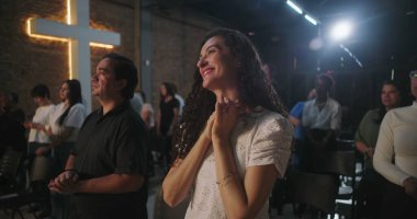 Hristiyan kilisesi etkinliği sırasında ayakta duran neşeli ifadeli cemaat üyeleri, arka planda parlayan bir haçla ruhlarını yansıtıyorlar.