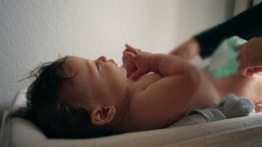 Bebek masasını değiştiriyor, anne kucağında bebek bezi, çocuk hafifçe gülümsüyor, rutin bakım, her gün ebeveyn ile etkileşim, rahatlık ve bakım, yakın ilişki..