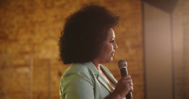 Podyumda tutkulu bir şekilde mikrofona konuşan bir kadın, ruhani dinleyicilere ilham verici bir mesaj veriyor, kendine güvenen bir lider ve inanç toplantısı sırasında güçlü bir bağlantı kuruyor.