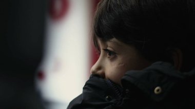 Ceketin üzerinde dinlenen genç bir çocuğun yakın çekimi, hareket halindeki otobüsün önünden geçen manzaraya bakmak, ciddi bir ifade, sessiz bir an, düşüncelere dalmış, derin bir düşünce.