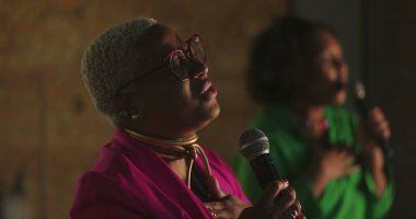 Şarkıcılar evanjelik kilise toplantısı sırasında tutkuyla şarkı söylerler, Afrikalı kökenli kadınlar mikrofon tutarlar, kalpten ibadet ederler, ruhsal ses iletimi, ruhsal bağlantı.