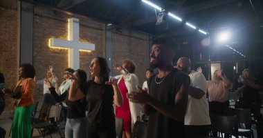 Kiliseye ibadet sırasında alkış tutan ve gülümseyen çok kültürlü cemaat, arka planda aydınlatılmış haç, inanç, neşe, birlik ve ruhani bağlılık ifadeleri.