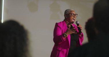 Sözcü tutkulu bir şekilde dinleyicilere hitap ediyor, mikrofonu tutuyor, vurgu için elini işaret ediyor, güçlü vaaz dağıtımı, çeşitli cemaatler dikkatlice dinliyor, ruhani olay