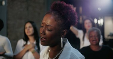 Kiliseye ibadet ederken tutkulu bir şekilde şarkı söyleyen kadın, maneviyatla anlamlı ve duygusal bir bağ içinde, cemaatin duacı birliğiyle çevrili.