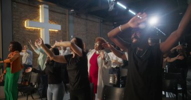 İbadet sırasında sevinçle el kaldıran ve dans eden farklı bireylerden oluşan bir grup, arka planda aydınlanan haç, canlı bir manevi bağlantı anı ve kutlama anı.