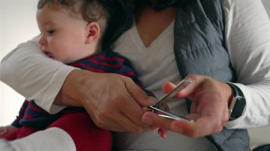 Anne, bebeğin tırnaklarını dikkatlice keserken kucağında kişisel bakım, bakım, bakım ve odaklanmış ebeveynlik yapıyor..