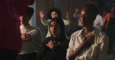 Ruhsal toplantı sırasında dua eden cemaat, eller kalplerin üzerinde, inanç ve sadakati ifade eden çeşitli gruplar, arka planda aydınlık haç ile kutsal ibadet anı