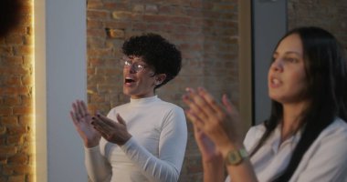 Çeşitli bireylerden oluşan bir grup, ilham verici bir iç etkinlik, neşeli ifadeler ve paylaşılan topluluk ruhu sırasında birlikte alkışlayarak, başarıyı veya başarıyı kutluyor.