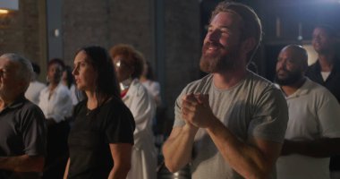 Derin dualarda çeşitli gruplar, elleri ön planda birbirine kenetlenmiş, yoğun bir bağlılık gösteren, ruhani bir toplantıda ibadet eden insanlarla çevrili insanlar.