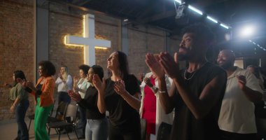 Kilisede ibadet sırasında alkışlayan ve gülümseyen çeşitli insanlar, arka planda parlayan haç, neşe, birlik ve ruhsal bağlantı ifadeleri
