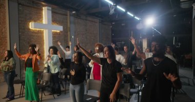 Çeşitli cemaatler kilise ayini sırasında el kaldırıyor, arka planda haç ışığı, ruhsal bağlantı ve kutsal mekanda kolektif bağlılık.