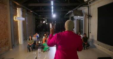 İbadet sırasında cemaate seslenen konuşmacı, izleyiciler sıraya dizilmiş, tuğla bir duvarda yanan haç dingin ve ilham verici bir atmosfer yaratıyor.