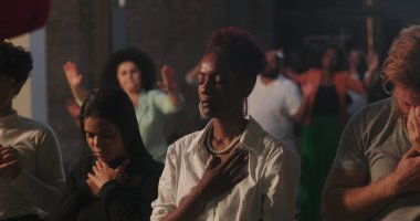 Manevi toplantı sırasında elleri göğsünde dua eden bir adam, çeşitli cemaatlerle çevrili, yanında dua eden Afrikalı Amerikalı bir kadın, inanç ve bağlılık vurgulandı