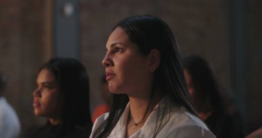 Odaklanmış ifadeye sahip bir kadın, ruhsal olay sırasında dikkatle dinliyor, dinleyicilerin arasında, huzurlu ve yansıtıcı bir inanç ve bağlantı anı yaşıyor.