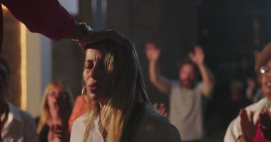 Vaiz, dua ederken ellerini kaldırmış bir kadını kutsar. Çeşitli cemaatlerle çevrili derin bir duygusal dua anı. Ruhlar aleminde kutsal bir atmosfer.