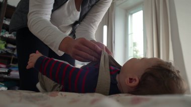 Anne bebek tulumlarını bağlıyor, bebek yatakta sakin kalırken kayışları ayarlıyor, günlük rutin rutin işlerinde rahat bir evde bakım ve bakım yapıyor..