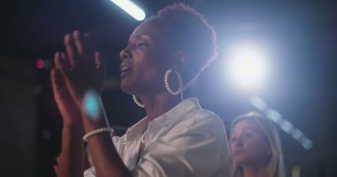 İbadet eden kadın, inancın duygusal ifadesi, ruhani kutlama, Hıristiyan buluşması, Afrika kökenli, neşeli bir birlik içinde birlikte övgüler yağdıran topluluk.