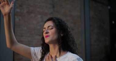 Kadının ibadet ederken el kaldırması, kilise ayini sırasında inancın ve bağlantının huzurlu ifadesi, duygusal ve ruhani bağlılık.