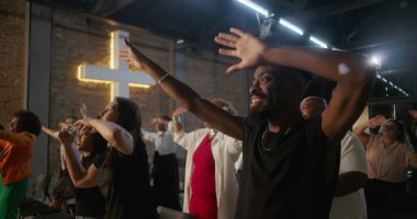 Çeşitli gruplar kilise ayini sırasında el kaldırıyor, arka planda çapraz aydınlanma, övgü, neşe ve ruhsal bağlantı ifadeleri.