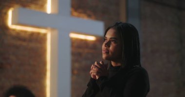 Derin dua eden İspanyol bir kadın, sakin bir ifade, elleri sımsıkı bağlanmış, arka planda parlayan haç ruhaniliği, umudu ve kiliseye ibadet sırasında inançla olan bağlantıyı simgeliyor.