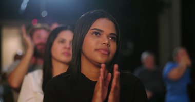 Çeşitli insan grupları bir kilise etkinliğinde seyircileri alkışlıyor, takdir ve katılımlarını gösteriyorlar, diğer insanlar arka planda alkışlıyorlar.