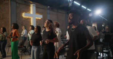 Kiliseye ibadet sırasında alkış tutan ve gülümseyen çok kültürlü cemaat, arka planda aydınlatılmış haç, inanç, neşe, birlik ve ruhani bağlılık ifadeleri.