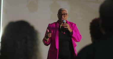 Sözcü tutkulu bir şekilde dinleyicilere hitap ediyor, mikrofonu tutuyor, vurgu için elini işaret ediyor, güçlü vaaz dağıtımı, çeşitli cemaatler dikkatlice dinliyor, ruhani olay