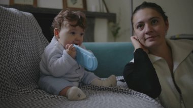 Bebek koltukta oturuyor, nesneleri çiğniyor, duyusal keşiflerle meşgul olurken anne başka tarafa bakıyor, erken çocukluk gelişimine odaklanmış çevreyi besliyor..