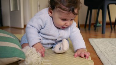 Bebek paspasın üzerinde oturuyor, ellerle çevreyi keşfediyor, merak ve odak ile dokunsal oyunlara girişiyor, ev ortamında erken çocukluk gelişimi.