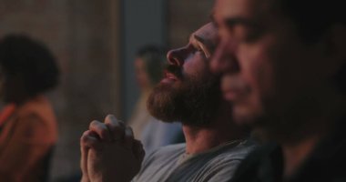Kızıl sakallı bir adam ibadet ederken ellerini kaldırıyor, adanmışlık, derin ruhsal bağ ve bir grup toplantısı sırasında gönülden dua eden bir adam.